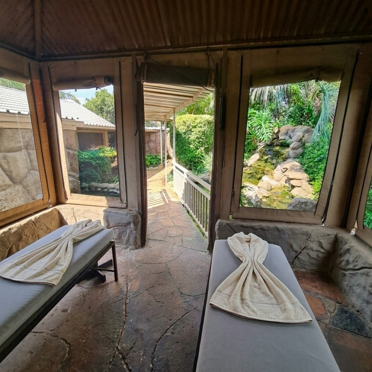 Tranquil dual massage treatment room at Crystal Rose Lodge with thatched ceiling, stone floors and garden waterfall views near the Cradle of Humankind area
